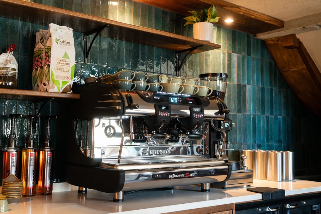 Image of The Farmers Boy coffee station with barista coffee machine with a tiled blue wall in the background and open shelving displaying the various coffee beans and loose leaf tea products available