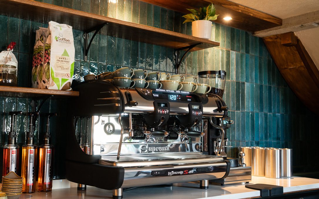 Image of The Farmers Boy coffee station with barista coffee machine with a tiled blue wall in the background and open shelving displaying the various coffee beans and loose leaf tea products available