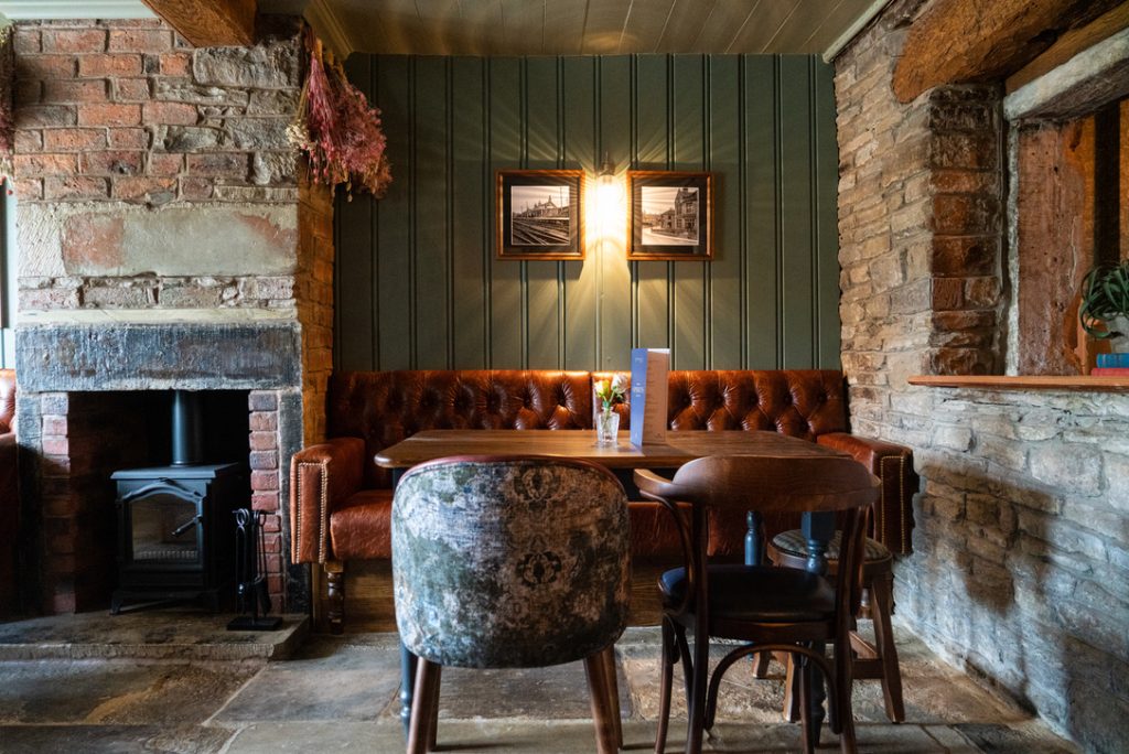 The Farmers Boy snug - soft lighting with wood panelled wall, leather banquet seating and a heritage-style open fireplace with a wood burning stove