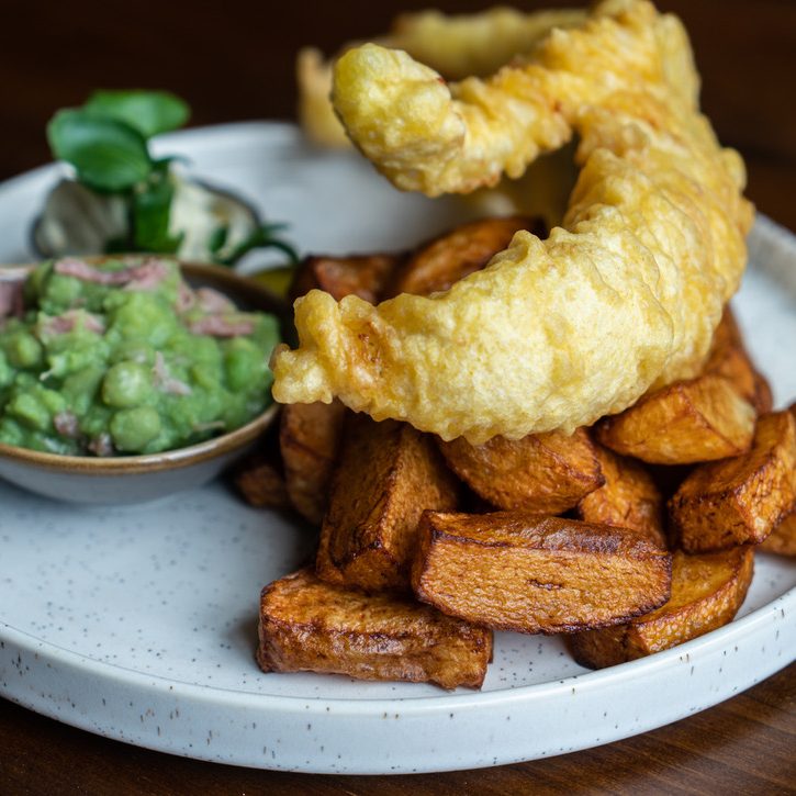 Beer-batterred Haddock & Chunky Chips from The Farmers Boy, Shepley served with ham hock mushy peas on a white stoneware dinner plate
