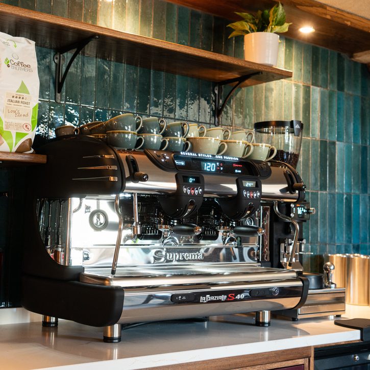Image of The Farmers Boy coffee station with barista coffee machine with a tiled blue wall in the background and open shelving displaying the various coffee beans and loose leaf tea products available